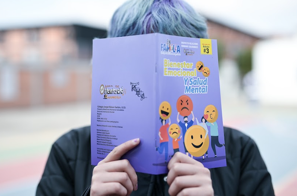 Estudiante sostiene libro sobre salud mental, tapándose el rostro.