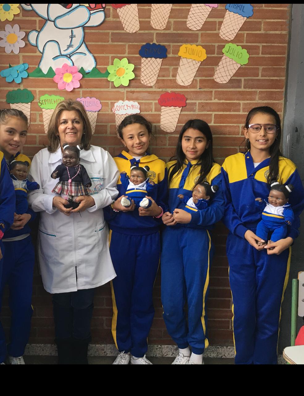 La profe Carmenza y sus estudiantes cargando muñecos