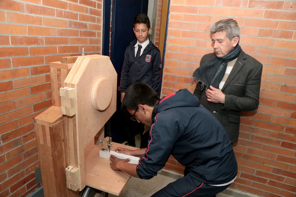 El rpofe Hugo con dos estudiantes y la máquina de madera