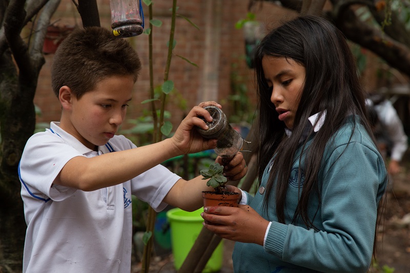 dos estudiantes colocando tierra en una matera